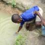 Young boy draws dirty water from pond